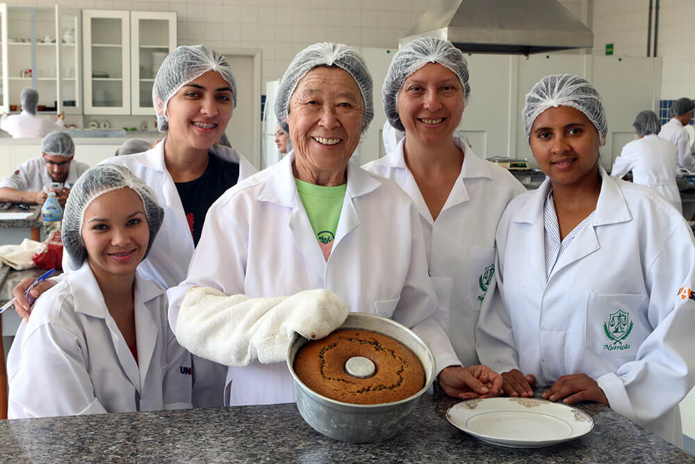 Acompanhada de colegas de classe no curso de Nutrição, dona Seetuko (ao centro) participa de uma aula de cozinha experimental no laboratório de técnicas dietéticas do Unasp, campus São Paulo. Créditos da imagem: Murilo Pereira